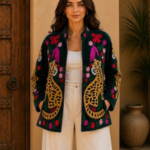 May include: A dark green velvet jacket featuring vibrant embroidery of yellow leopards with black spots, accented by pink and red floral patterns. The jacket has a high collar, long sleeves, and two front pockets, worn over a white top and cream trousers.