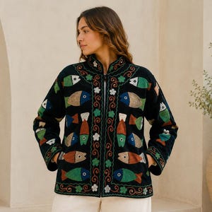 Könnte beinhalten: Eine schwarze Langarmjacke mit einem lebendigen Stickmuster aus bunten Fischen in Grün-, Blau- und Orangetönen, akzentuiert durch kleine weiße Blumen und rote, geschwungene Rankenmotive entlang der Vorderseite und am Stehkragen.