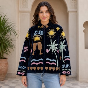 Könnte beinhalten: Eine dunkelblaue Samtjacke mit bunten Stickmotiven, darunter gelbe Sonnen, Palmen, rosa Blumen, Wellenlinien, braune Herzen und Champagnergläser. Das Wort sun ist in Hellblau gestickt, ebenso wie das Wort moon an der unteren Ärmelkante.