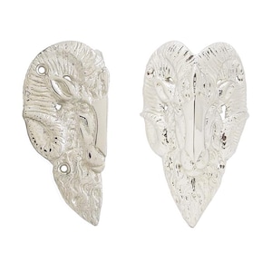 May include: Two silver-toned metal hardware pieces shaped like ram heads. The left piece is shown in profile with two circular screw holes, while the right piece is shown from a front-facing perspective, both featuring detailed horns and fur texture.