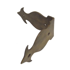 May include: An L-shaped brass corner bracket featuring a decorative, curved silhouette with pointed ends. The metal hardware has a muted, aged finish and includes three pre-drilled circular holes for mounting purposes on furniture or wooden boxes.