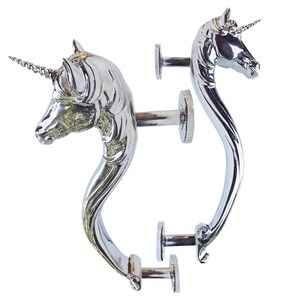 May include: Two silver-toned metal door handles, each featuring a sculpted unicorn head at the top with a prominent spiral horn. The handles have a curved, elongated neck design and are attached to circular mounting plates for installation.