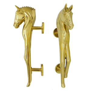Puede incluir: Un par de manijas de puerta de latón pulido, cada una con un diseño esculpido de cabeza y cuello de caballo. Las manijas están orientadas verticalmente con dos placas de montaje circulares que se extienden desde la parte posterior.