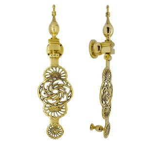 May include: A polished brass door knocker featuring a vertical design with a central openwork circular motif, intricate fan-shaped detailing, and a pointed finial at the top. The hardware includes a circular mounting plate and a small bottom knob.