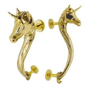Puede incluir: Dos manijas de puerta de latón pulido, cada una con una cabeza de unicornio esculpida en la parte superior. Las manijas tienen un diseño de cuello curvo y alargado que se extiende hacia abajo hasta una placa de montaje circular.