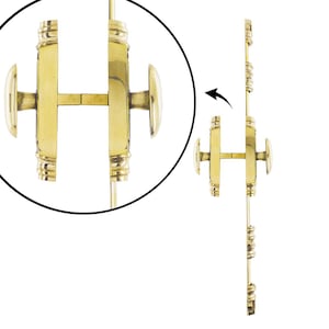 Può includere: Un set di chiusura a cremonese in ottone lucido con un'asta verticale caratterizzata da dettagli decorativi a coste e due pomelli ovali. Il meccanismo include un alloggiamento centrale con un sistema di bloccaggio scorrevole per porte doppie.