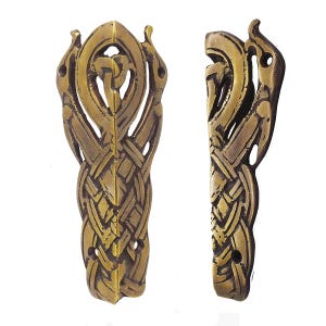 May include: Two brass-colored metal corner guards featuring an intricate, raised woven pattern and a central knot design. Each piece has a pointed top and two circular screw holes at the base for mounting, displaying a metallic finish with dark accents.