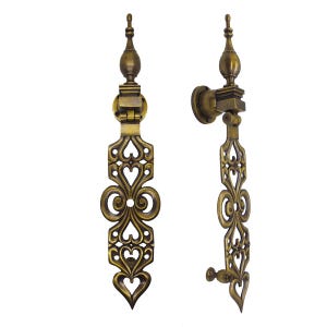 May include: Two antique brass door knockers featuring an elongated vertical design with intricate cut-out heart and scroll patterns. Each piece includes a top finial, a circular mounting plate, and a hinged drop section with a pointed base.