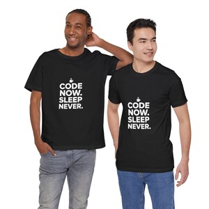 May include: A black short-sleeved t-shirt featuring white text that reads CODE NOW. SLEEP NEVER. with a small coffee cup icon above the text. The shirt has a crew neckline and a standard fit, displaying the graphic clearly on the chest area.