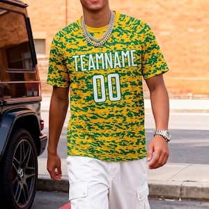May include: A short-sleeve crew neck t-shirt featuring a yellow and green camouflage-style pattern. The front displays the text TEAMNAME in white block letters above the number 00 in a matching white font with a thin green outline.