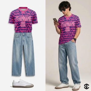 May include: A short-sleeve crew neck t-shirt featuring a pink and blue camouflage pattern with the text TEAMNAME and the number 00 in white, paired with light-wash blue denim jeans and white sneakers with light grey suede toe caps.