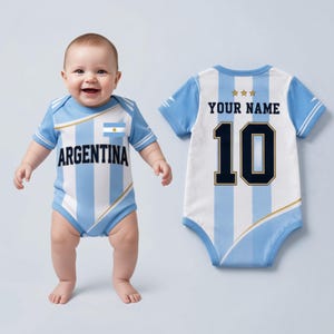 Puede incluir: Un body para bebé con los colores de la bandera argentina de rayas verticales azul claro y blancas. El frente muestra la palabra ARGENTINA y una pequeña bandera. La parte posterior muestra tres estrellas doradas, el texto YOUR NAME y el número 10 en azul oscuro.