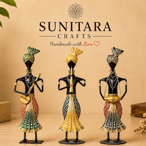 May include: Three metal musician figurines standing on circular bases. Each figure wears a turban and a patterned skirt. The left figure plays a stringed instrument, the center plays a flute, and the right plays a drum. Text reads SUNITARA CRAFTS.
