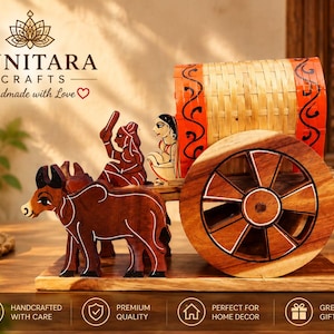 May include: A wooden decorative bullock cart sculpture featuring two brown carved oxen pulling a cart with a woven bamboo roof and orange painted accents. The cart includes two small carved figures of people seated inside the structure.