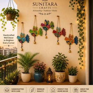 Pode incluir: Cinco decorações de parede de madeira em forma de pássaro pintadas à mão, com contas e sinos de latão pendurados. Cada pássaro apresenta padrões florais intrincados em azul, verde, vermelho e laranja, exibidos acima de plantas num terraço.