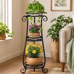 Op de afbeelding: Een zwarte metalen plantenstandaard met drie ronde niveaus en krulwerkdetails. De standaard bevat een groene bladplant op het bovenste niveau, een potplant met paarse bloemen op het middelste niveau en een potplant met gele bloemen onderaan.