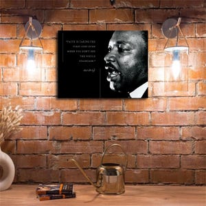 May include: A rectangular wall art print featuring a black and white portrait of Martin Luther King Jr. on the right and the quote Faith is taking the first step even when you don't see the whole staircase on the left in white text.