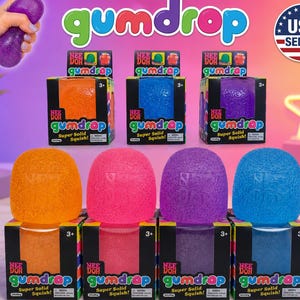 May include: A collection of Nee Doh Gumdrop squishy toys in orange, pink, purple, and blue, each featuring a textured surface and the embossed logo. The items are displayed both inside their individual square cardboard boxes and as loose units.