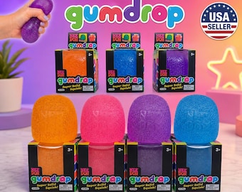 May include: A collection of Nee Doh Gumdrop squishy toys in orange, pink, purple, and blue, each featuring a textured surface and the embossed logo. The items are displayed both inside their individual square cardboard boxes and as loose units.