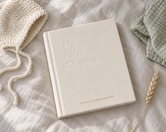 Puede incluir: Un libro de tapa dura de color crema con el texto en relieve My First Chapter y el texto impreso más pequeño A COLLECTION OF CHERISHED MILESTONES. Junto al libro hay un gorro de punto color crema con lazos y una tela de muselina verde salvia.