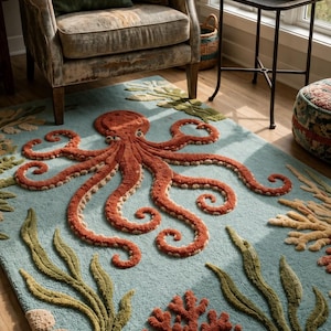 Op de afbeelding: Een rechthoekig vloerkleed met een lichtblauwe achtergrond en een grote, verhoogde, oranje octopus in het midden. Het ontwerp bevat getextureerd groen zeewier, koraalformaties in rood en beige, en kleine rotsachtige vormen langs de onderrand.