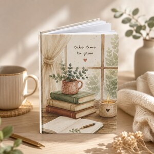Puede incluir: Un diario de tapa dura con una ilustración en acuarela de una pila de tres libros, una planta en maceta, una vela encendida y un cuaderno abierto con un bolígrafo. El texto "take time to grow" con un pequeño corazón está impreso en la portada.