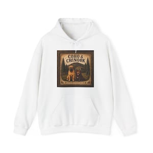 Puede incluir: Sudadera con capucha blanca con un estampado gráfico. El gráfico presenta el texto "COHO & CHINOOK" y una ilustración de dos perros en un bosque, enmarcada en marrón. La sudadera con capucha tiene un bolsillo delantero y una capucha con cordón.