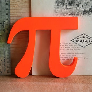 May include: A bright orange, three-dimensional pi symbol made of wood. The symbol is about 6 inches tall and is sitting on a wooden surface. The Etsy.com logo and the text "NorthStar50 Handmade" are visible in the background.