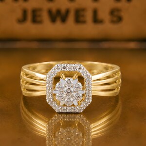 Peut inclure: Une bague en or avec une tête octogonale sertie de petites pierres claires entourant un groupe central de pierres rondes. L'anneau se compose de quatre fils d'or parallèles de chaque côté. Le texte MAYRA JEWELS est visible en arrière-plan.
