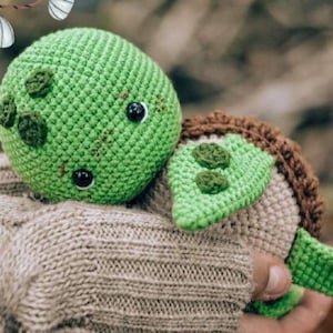 May include: A crocheted turtle toy with a bright green head featuring dark green spots and black plastic eyes. The turtle has a brown shell and light green flippers, crafted with a textured yarn stitch pattern throughout the entire body.