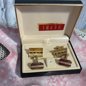 May include: A pair of gold cufflinks with red stones in a black box with the word "SWANK" printed in red on the inside of the lid.