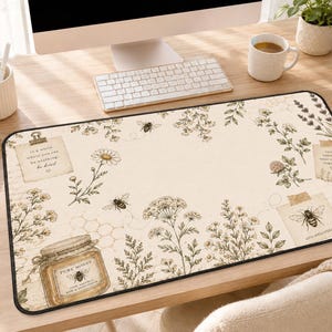 May include: A rectangular desk mat featuring a cream-colored background with botanical illustrations of wildflowers, bees, a jar of honey labeled Pure Honey, and paper notes with text including In a world where you can be anything be kind.