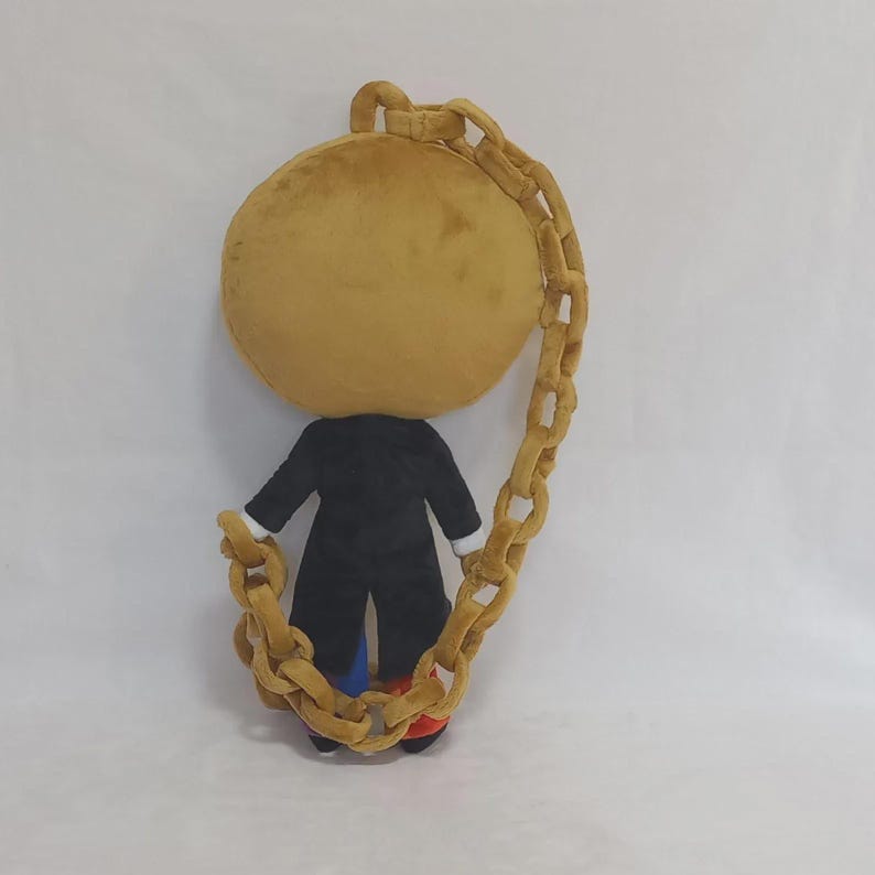 May include: A plush toy featuring a large, round, tan head and a black coat. The figure is encircled by a long, thick, tan plush chain that connects from the top of the head to the base, with small glimpses of blue and red fabric at the feet.