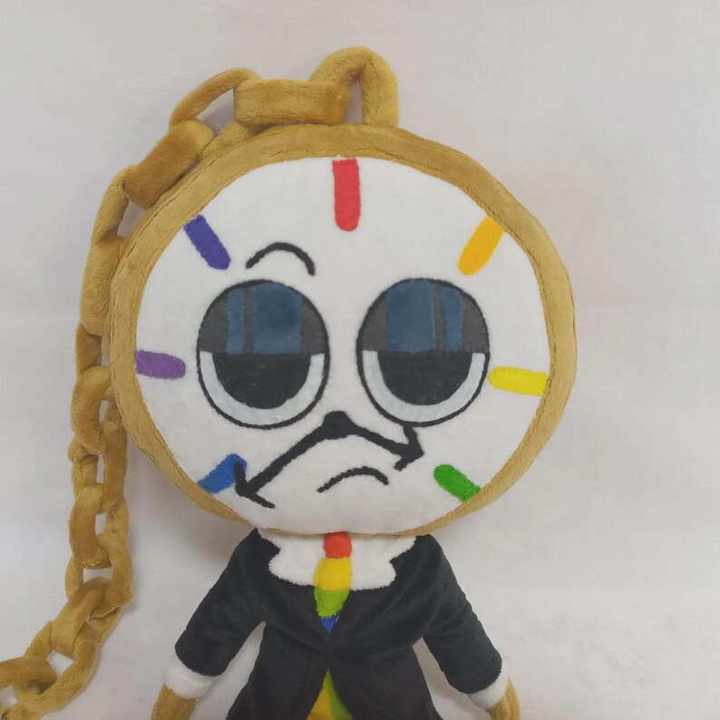 May include: A plush toy shaped like a clock with a round white face, large dark blue eyes, and a black clock hand mouth. It features a gold plush chain, a black suit jacket, and a colorful tie. The clock face has red, yellow, green, blue, and purple markers.