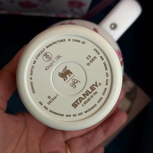 May include: The base of a cream-colored Stanley tumbler featuring a 40oz/1.18L capacity. The bottom includes the Stanley logo, a winged lion icon, a bow icon, and text stating it is BPA free, dishwasher safe, and designed in Seattle, WA.