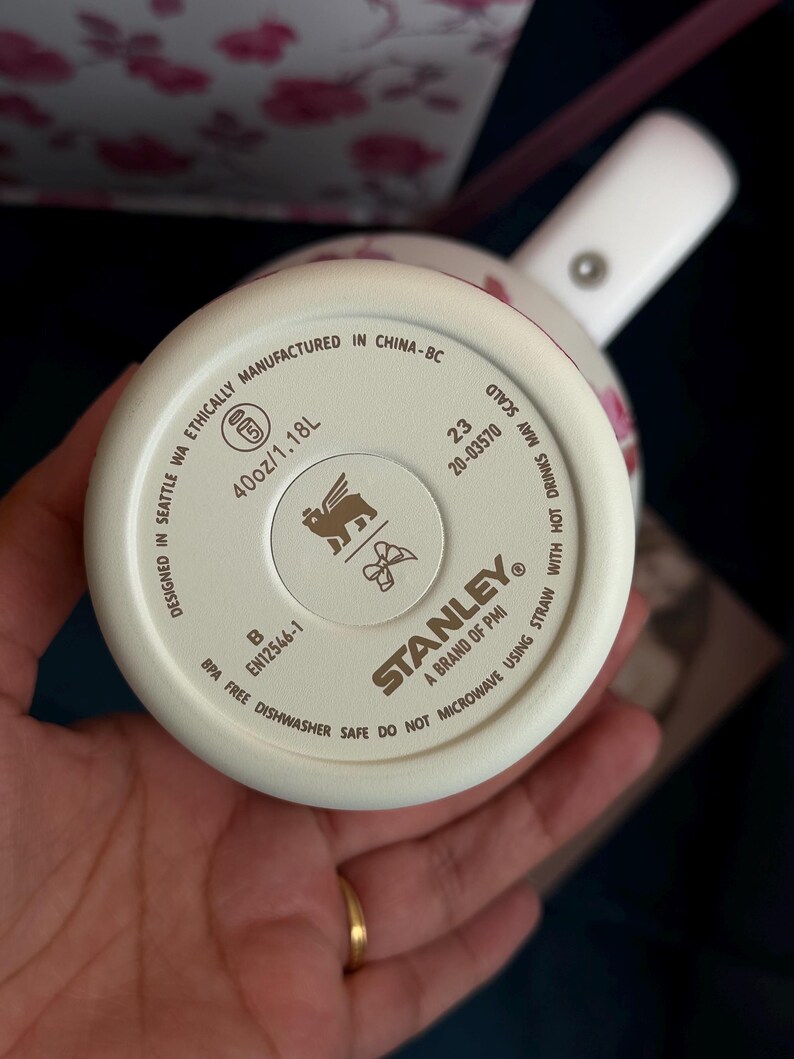 May include: The base of a cream-colored Stanley tumbler featuring a 40oz/1.18L capacity. The bottom includes the Stanley logo, a winged lion icon, a bow icon, and text stating it is BPA free, dishwasher safe, and designed in Seattle, WA.