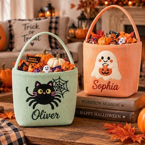 Puede incluir: Dos cubos de Halloween de pana con asas. El cubo verde claro presenta un gato negro y una telaraña bordados con el nombre Oliver. El cubo naranja presenta un fantasma blanco bordado sosteniendo una calabaza con el nombre Sophia.