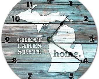 Könnte beinhalten: Eine runde Uhr mit einem blauen und grauen Holzmaserungsmuster. Das Zifferblatt der Uhr zeigt eine weiße Umrandung des Bundesstaates Michigan mit den Worten "Great Lakes State" und "home". Die Zahlen 1 bis 12 befinden sich am Rand des Zifferblatts.