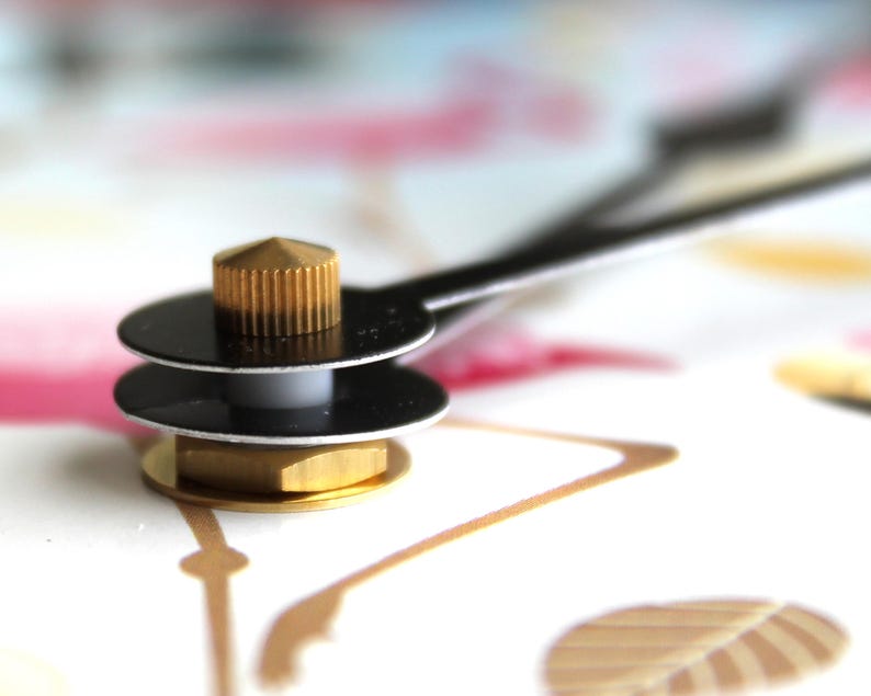 A close-up view of a metallic object with a golden-colored top, resting on a white surface with a pink and gold pattern.