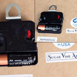 a black electronic device, possibly a clock, with a battery and a label indicating it is made in the USA.