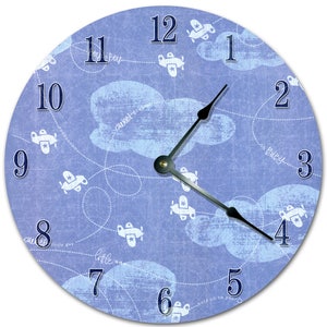 May include: A blue and white round clock with a whimsical design featuring airplanes flying through clouds. The clock face has Roman numerals and the words "sweet dreams", "oh baby", "little guy", "little one", and "hold on to your dreams".