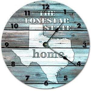 May include: A round wooden clock with a blue and white distressed woodgrain design. The clock face features a white outline of the state of Texas with the words "The Lone Star State" and "home" printed in white. The clock hands are black.