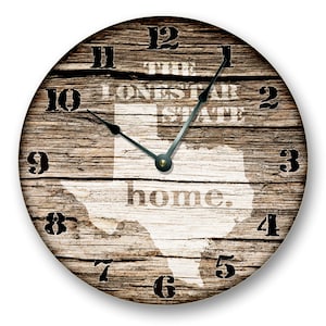 May include: Circular wall clock with a distressed wood effect. The clock face displays the Texas outline in white, with the text "THE LONE STAR STATE" and "home." in a vintage font. Black numerals and hands complete the design.