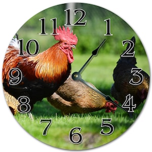 May include: Round wall clock featuring a rooster and hens in a grassy field. The clock face has black numerals and hands. The rooster has red comb and wattle, with brown and black feathers. The background is a blurred green.