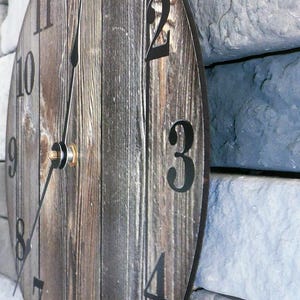 A wooden clock with black numbers on a stone wall.