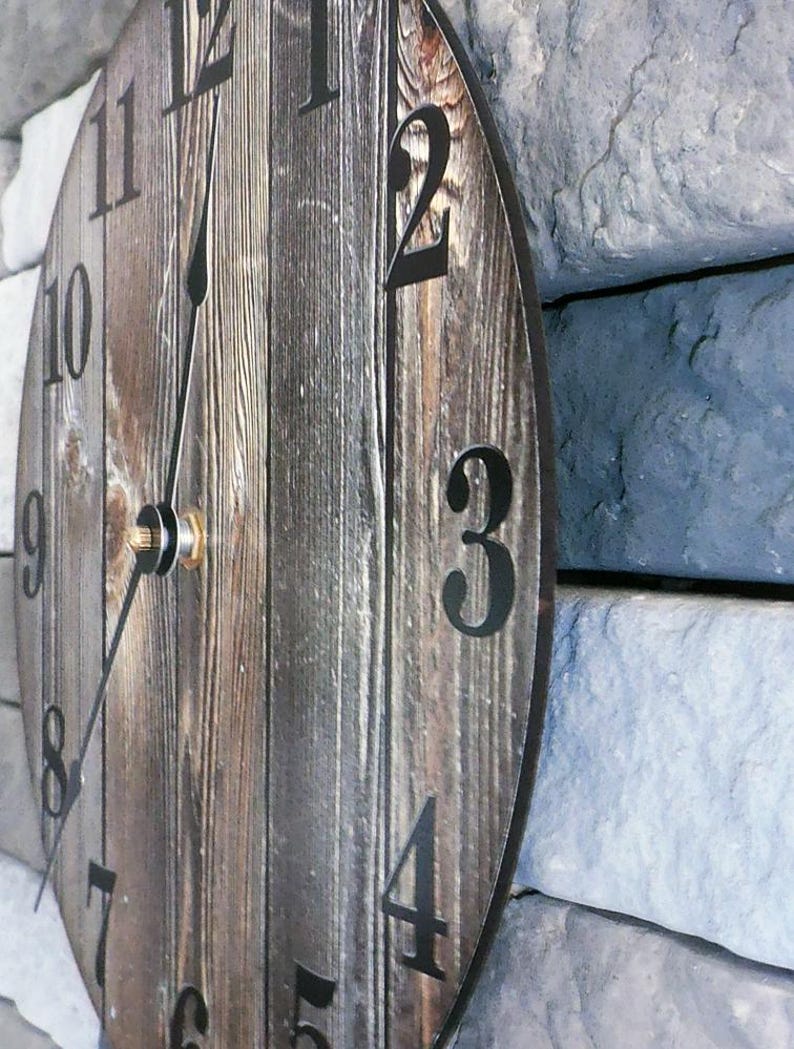 A wooden clock with black numbers on a stone wall.