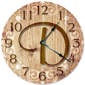May include: A round wooden clock with a brown woodgrain background and white floral accents. The clock face features a large brown letter "D" in the centre and brown numbers around the edge.