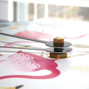 a close-up view of a clock mechanism with a pink and white floral pattern on the surface it is mounted on.