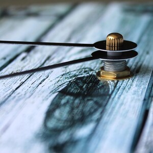 A close-up view of a metallic object with a golden-colored screw, resting on a wooden surface with a blurred background.