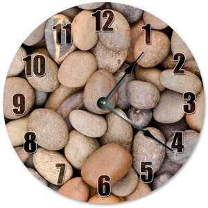 May include: Round wall clock featuring a natural stone design. The clock face is covered with various sized smooth, gray and brown river rocks. Black numerals mark the hours, and black hands indicate the time.
